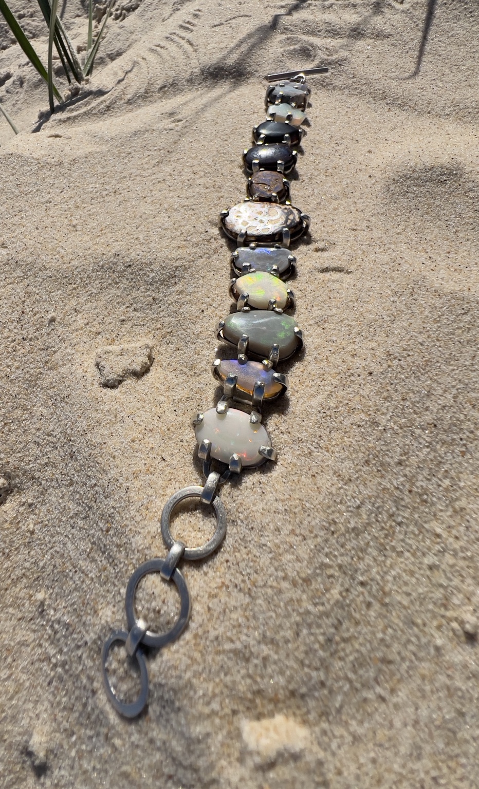 Bracelet composé d’opales de différentes mines australiennes, photographié sur le sable
